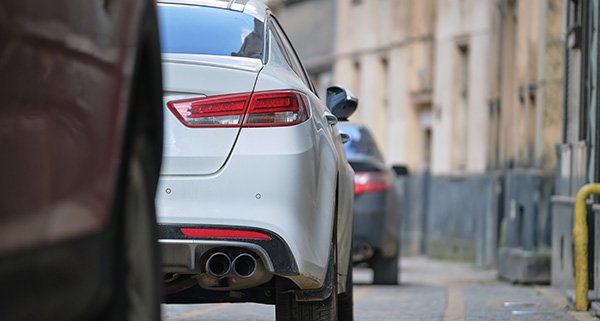 white car parked on street with visible exhaust pipes and blurred background vehicles including sporty models highlighting 13 reasons for car choice