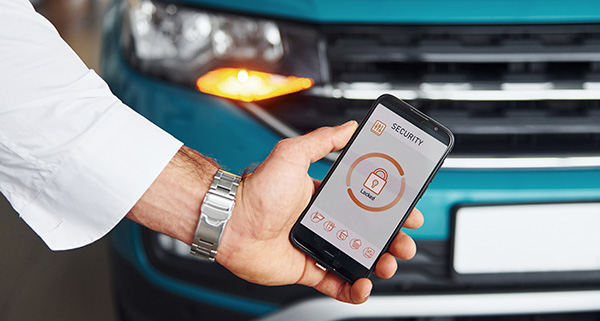 hand holding smartphone displaying security app interface near a parked vehicle showcasing advanced features for 15 car models