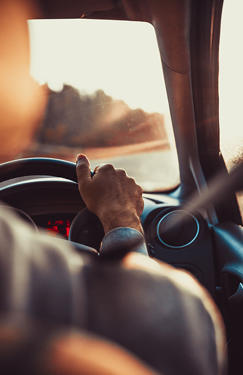 a hand gripping a steering wheel inside a car while driving on a scenic road at sunset 10 driving tips for better journeys