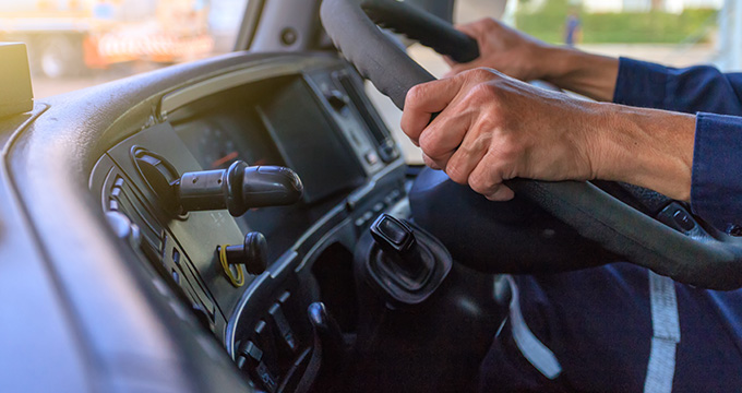 hands gripping a steering wheel inside a vehicle dashboard with controls for navigation and gear shift focusing on driving safety and efficient operation of three key vehicle functions